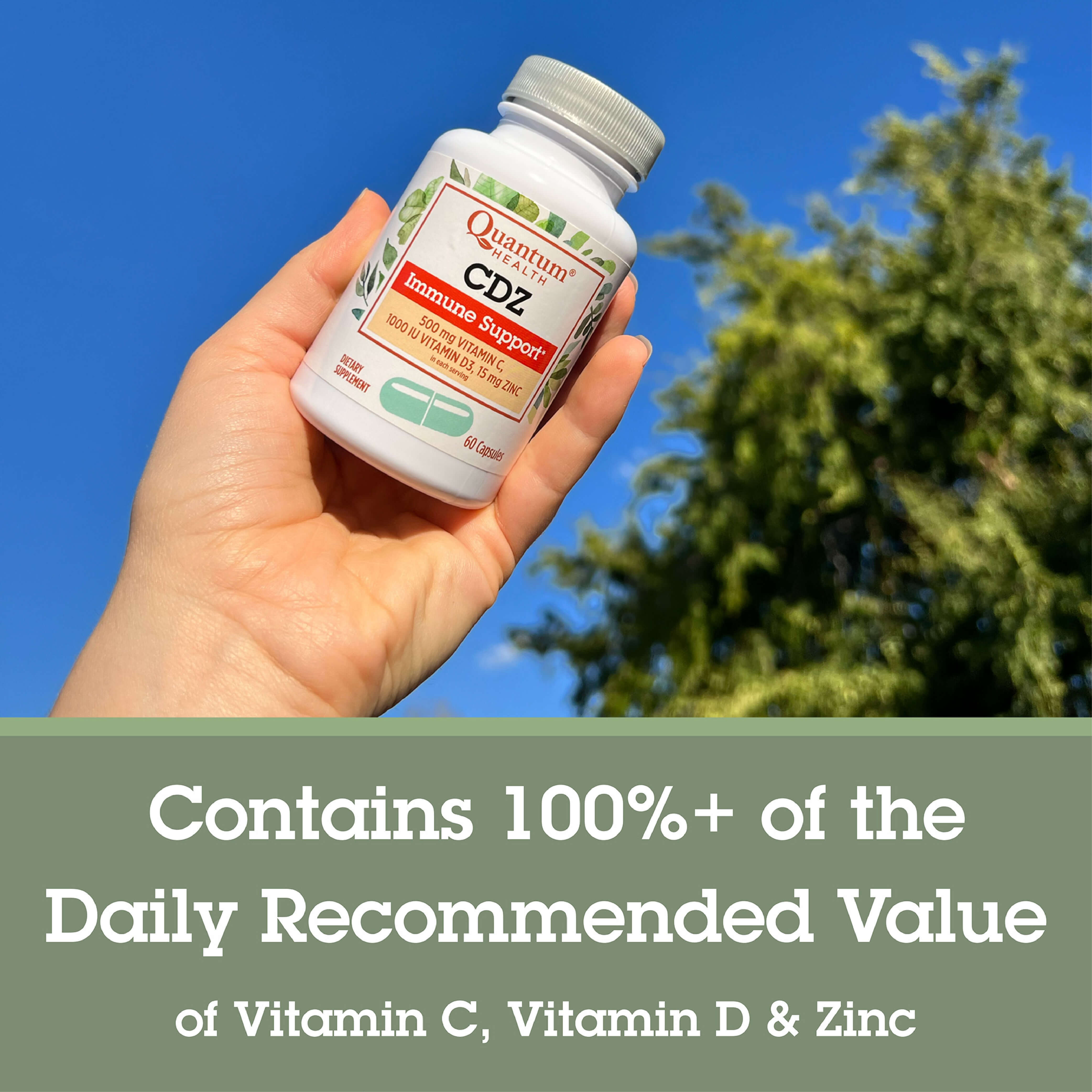 Hand holding a bottle of Quantum Health CDZ supplement with a clear blue sky and green trees in the background.