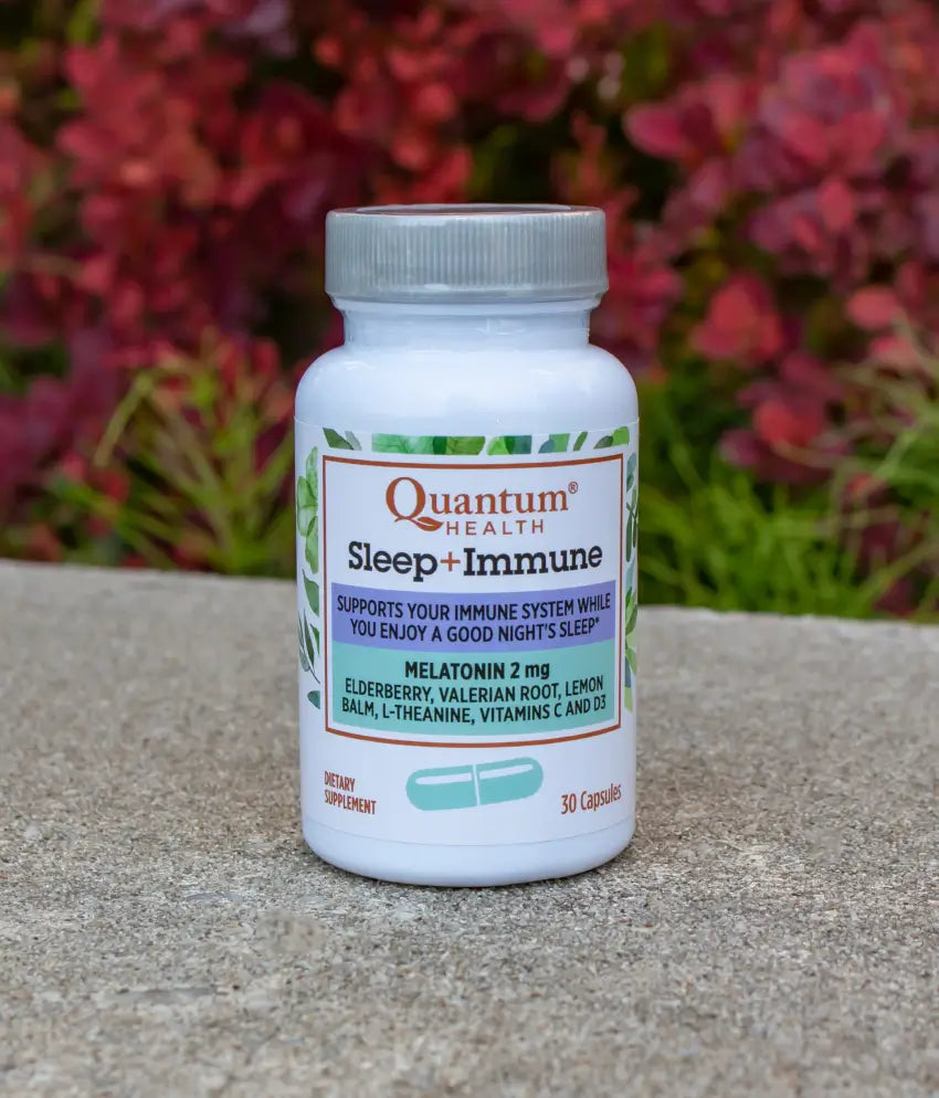 Quantum Health Sleep + Immune supplement bottle on a concrete surface with blurred red flowers in the background